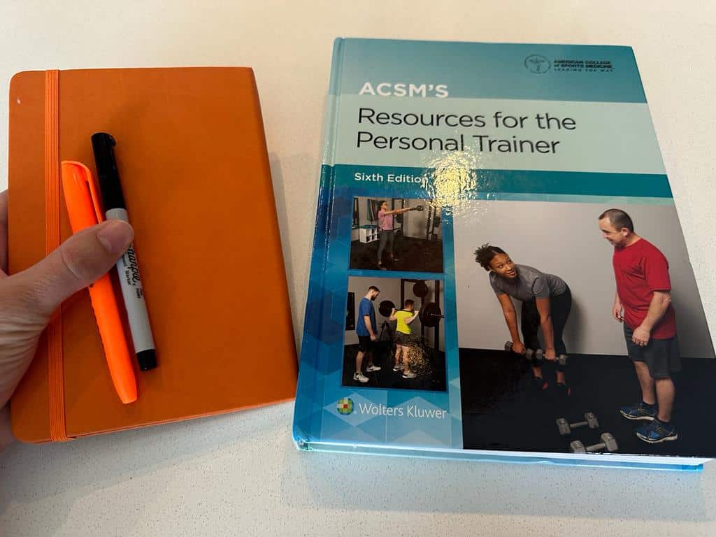 ACSM CPT textbook cover with a journal and study materials ready to go to the left