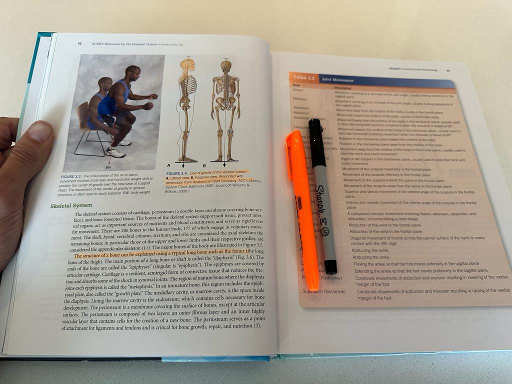 ACSM CPT textbook open and showing highlighted text from studying with the pen and highlighter to the side.