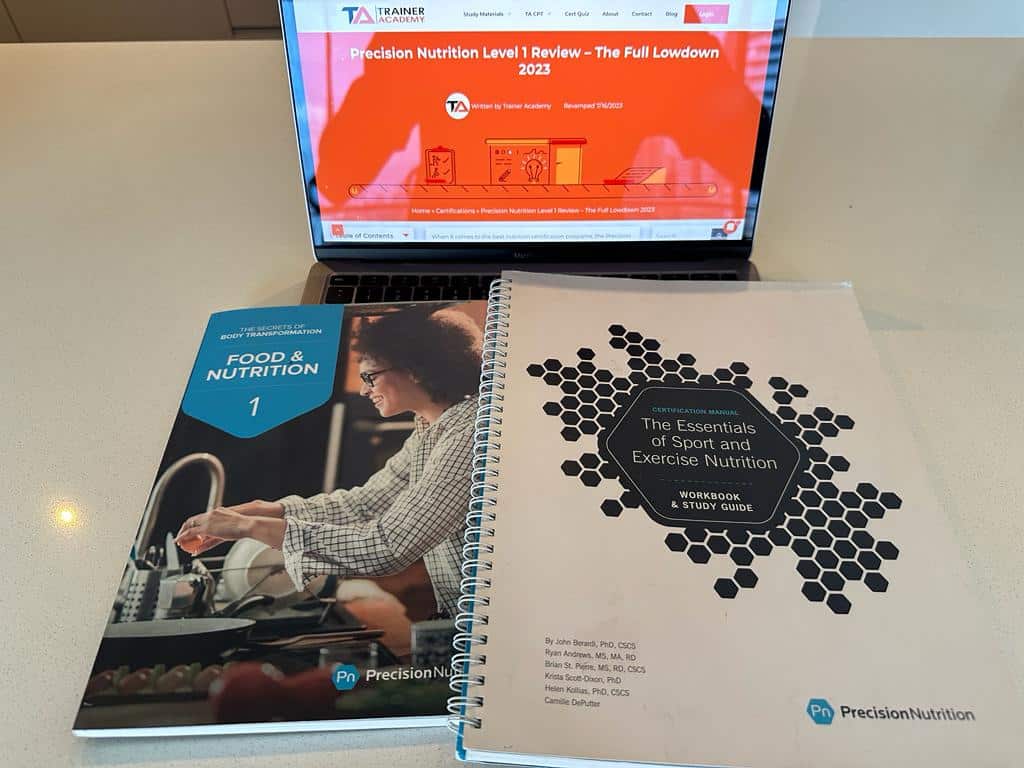 https://traineracademy.org/wp-content/uploads/2023/08/Both-of-the-precision-nutrition-textbooks-with-their-covers-shwoing-and-a-laptop-showing-the-review-for-the-certification.jpeg