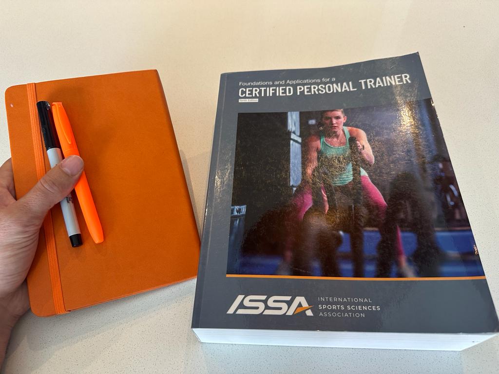 ISSA CPT textbook showing off the cover along with a journal, sharpie, and highlighter