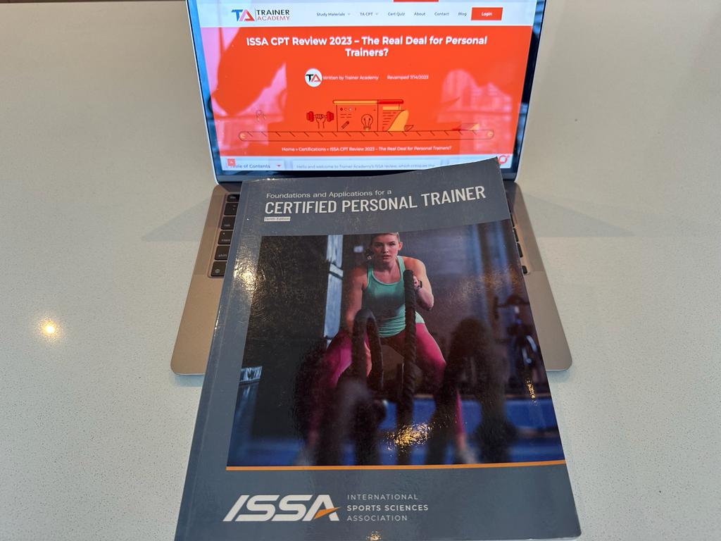 ISSA CPT textbook with the cover showing and on top of a laptop showing the ISSA CPT review