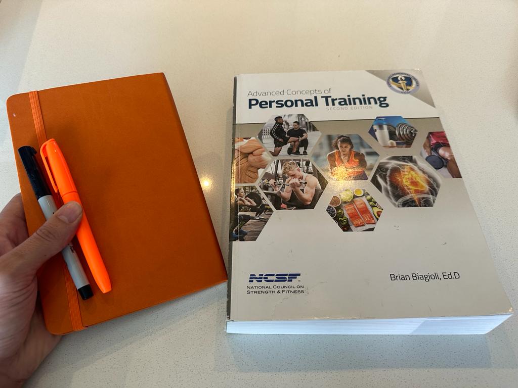 The NCSF personal training textbook showing the cover and with a learner preparing to use a journal, highlighter, and pen